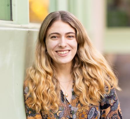 Headshot Aviva Intveld, leaning against a pale green wall and smiling. Photo: Steph Stevens