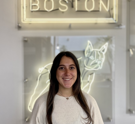 Headshot of Mackenzie Griffith with a light neon sign in the back that says Boston and a french bulldog