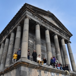 13 MIT students on the platform of the Temple of Garni in Yerevan, Armenia, seating and leaning against the large columns 