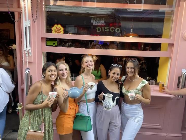 Anjali Chadha standing in front of a pink store with 4 other friends holding some teapots and teacups