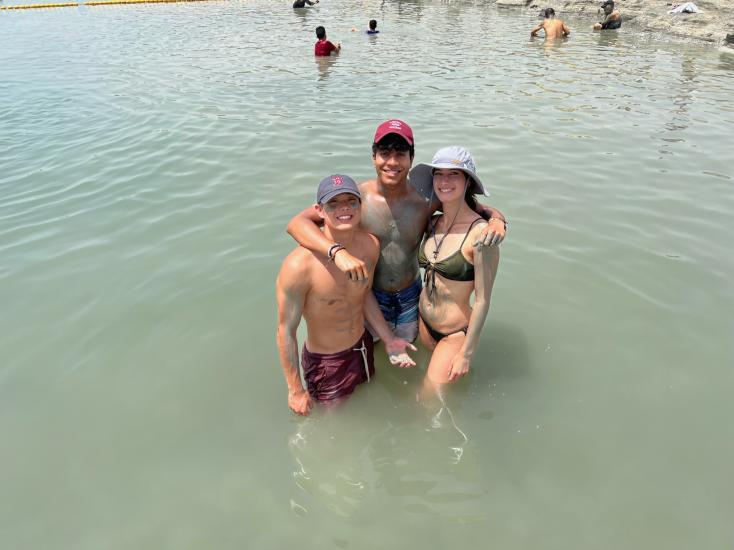 Yajvan Ravan in a red cap with his arms around two other MIT students in the Dead Sea