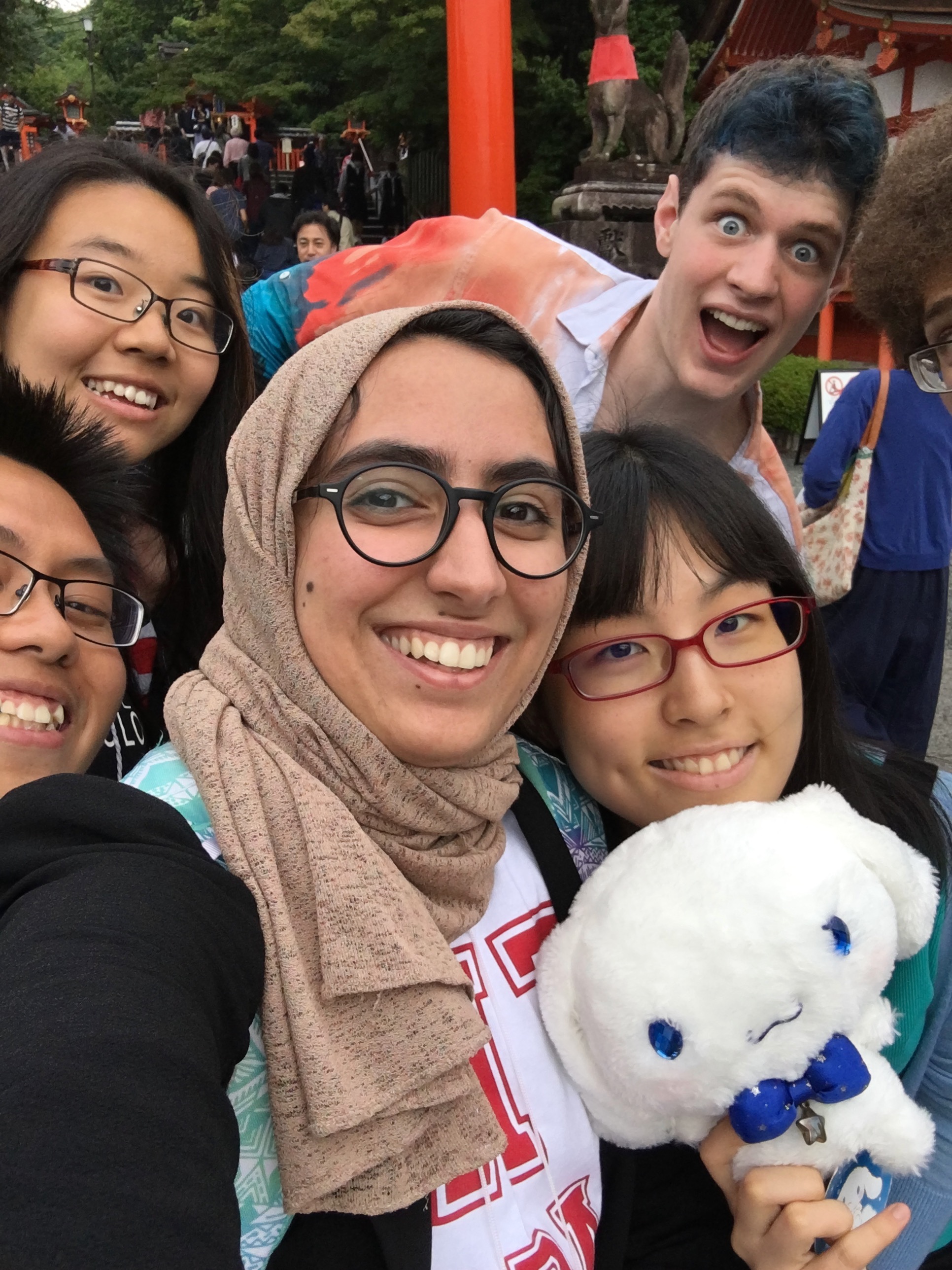 A selfie of Marwa AlAlawi with four other MIT students with a sea of people in the back and part of the Japanese cylindrical shrine