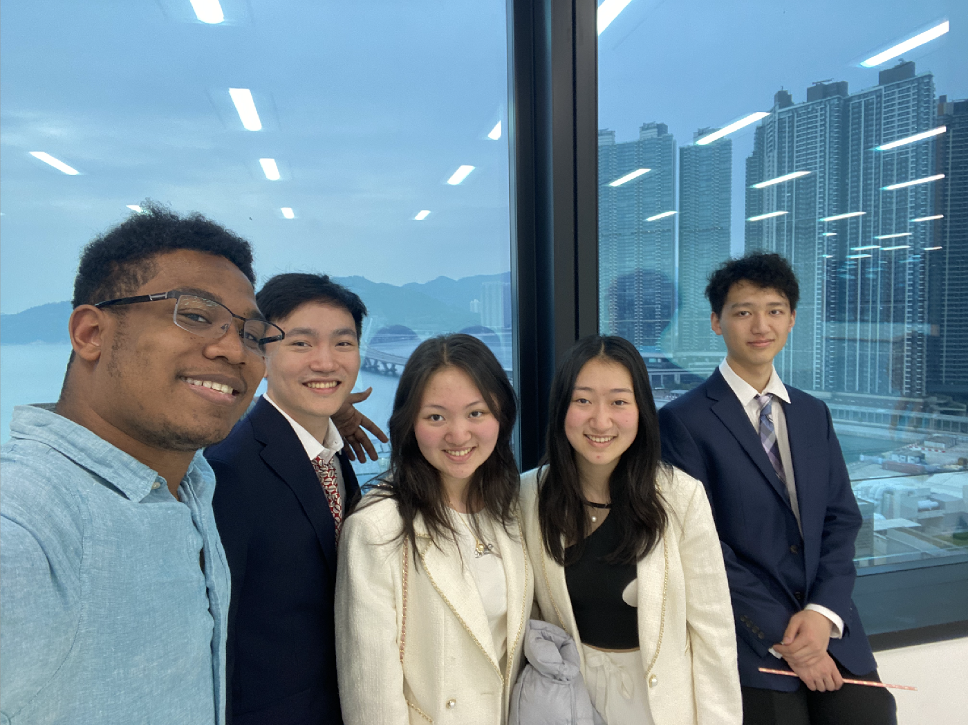 A selfie taken by Zachary Francis with his teammates in Hong Kong with a glass window in the background overlooking Hong Kong's skyline