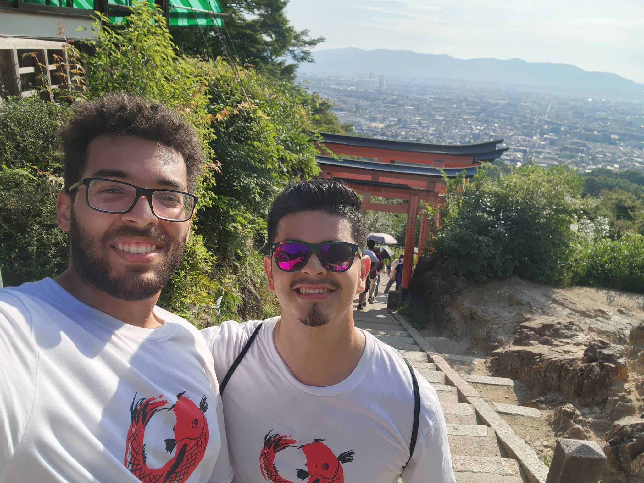 Selfie of Arthur De Los Santos and Daniel from MIT on the steps with a Japanese torii gate in the background and the city skyline