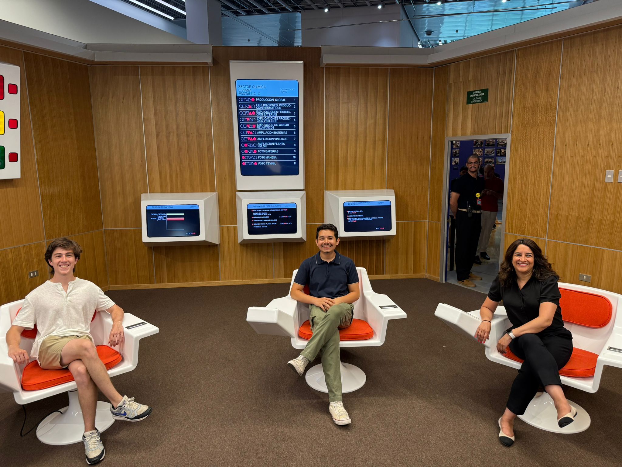 Fernando Oliver seated on the far left with two other MIT representative in a room with wood panels and screen hung to it