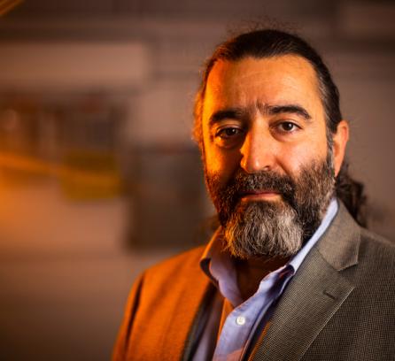 Headshot of Areg Danagoulian in a suit, dark background and ray of orange light illuminating Areg's face from the left