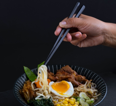 person holding chopsticks with bowl of ramen