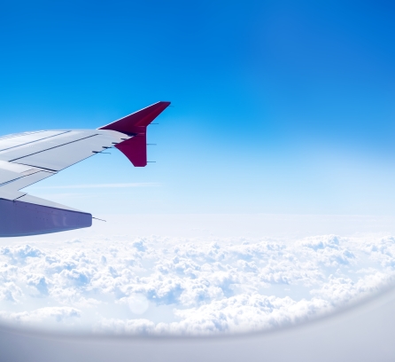 View from airplane window with airplane wing with a deep blue sky and fluffy clouds below