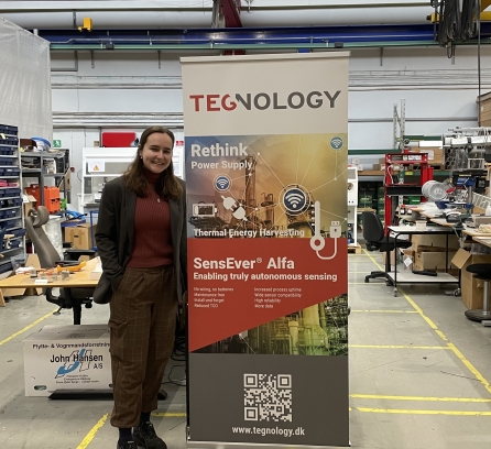 Dahlia stands next to Tegnlogy poster in the lab