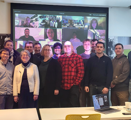 14 people standing in front of a projector of a gallery of Zoom attendees