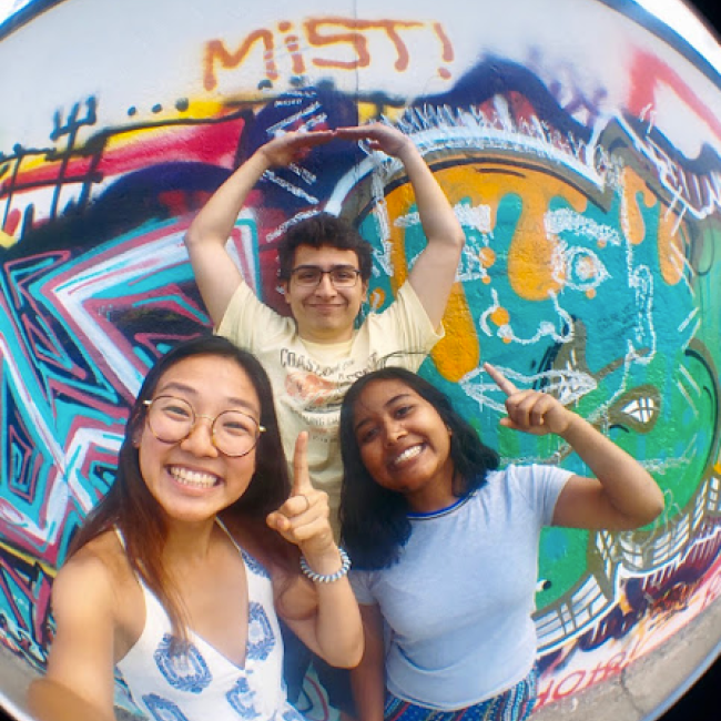 Three student interns standing in front of a graffiti wall