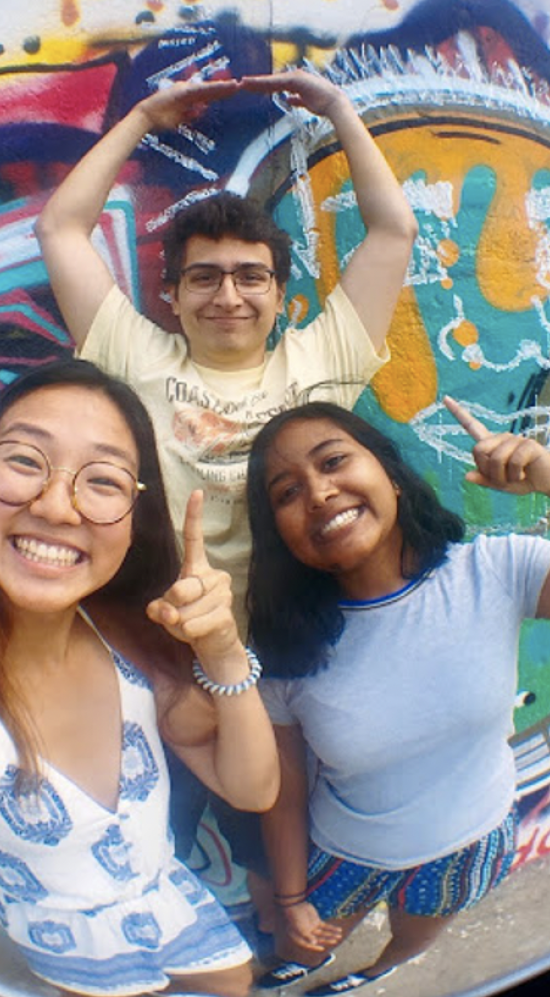 Three student interns standing in front of a graffiti wall