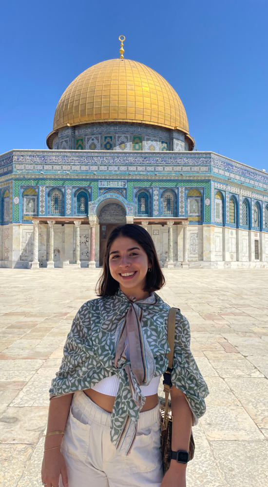 Headshot of Adriana Rivera Socarras with the Dome of the Rock, an Islamic shrine with a gold dome, in Jerusalem, in the background