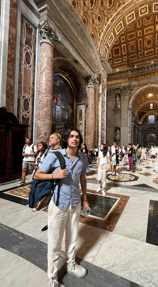 Diego Yanez-Laguna standing inside the Atrium of St. Peters Basilica with red-brown round columns and an arch ceiling with a Baroque-style design