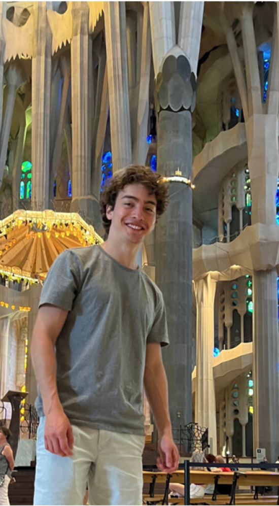Santiago Vazquez pictured in a church with, tourists, tall grey columns and colorful stained glass in the background