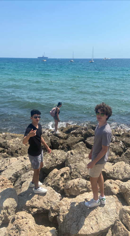 Santiago Vazquez and 2 MIT students standing on rock formations on the beach at Palma, Mallorca with the sea in the background and some boats in a distance