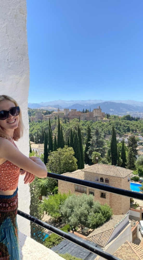 Sierra Greene smiling at the camera while leaning on a railing of the bell tower overlooking La Alhambra in Granada