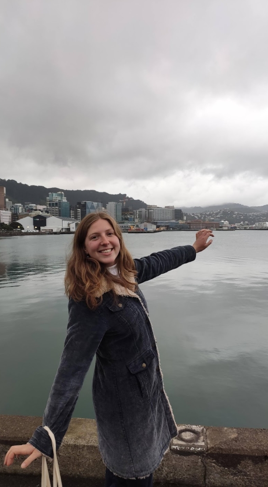 Emily Levenson posing with the waterfront promenade in the background in Wellington, New Zealand on a cloudy day