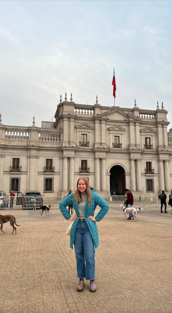 Mikayla Britsch standing in front of a fenced Palacio de Moneda in Chile with a group of greyhound owners protesting dog racing