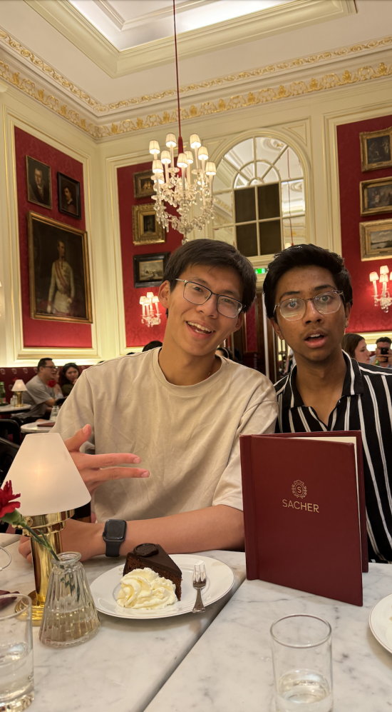 Andy Zheng seated with a friends at a marble table with a red menu upright and two plates of chocolate cake with cream
