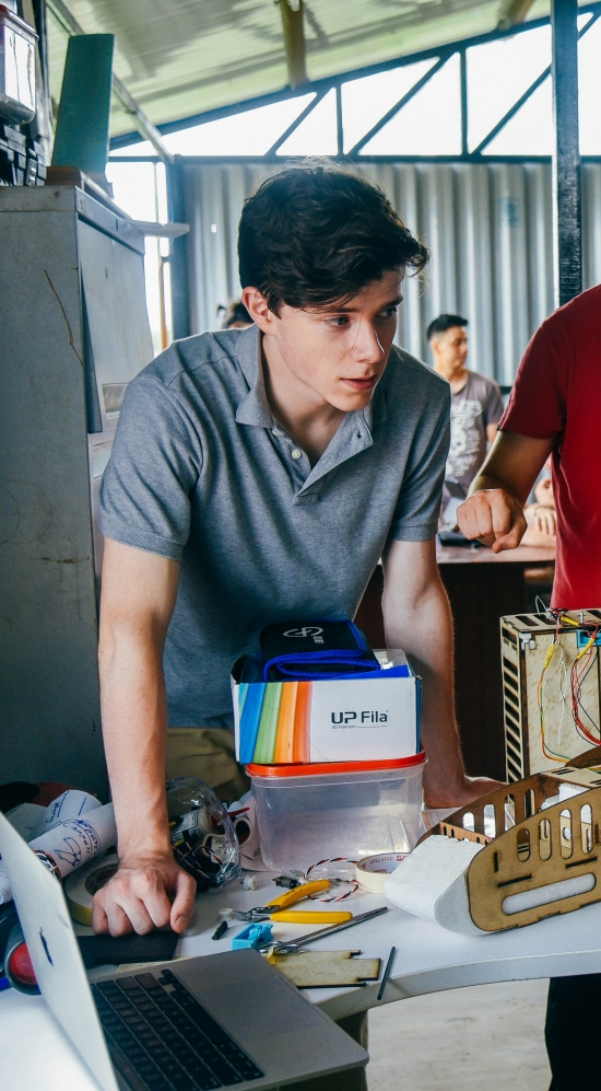 Josiah Shimandle leaning over a table with Marc Vidal standing next to him with two hands at a 90 degree motioning something to someone seated at the table looking up to them