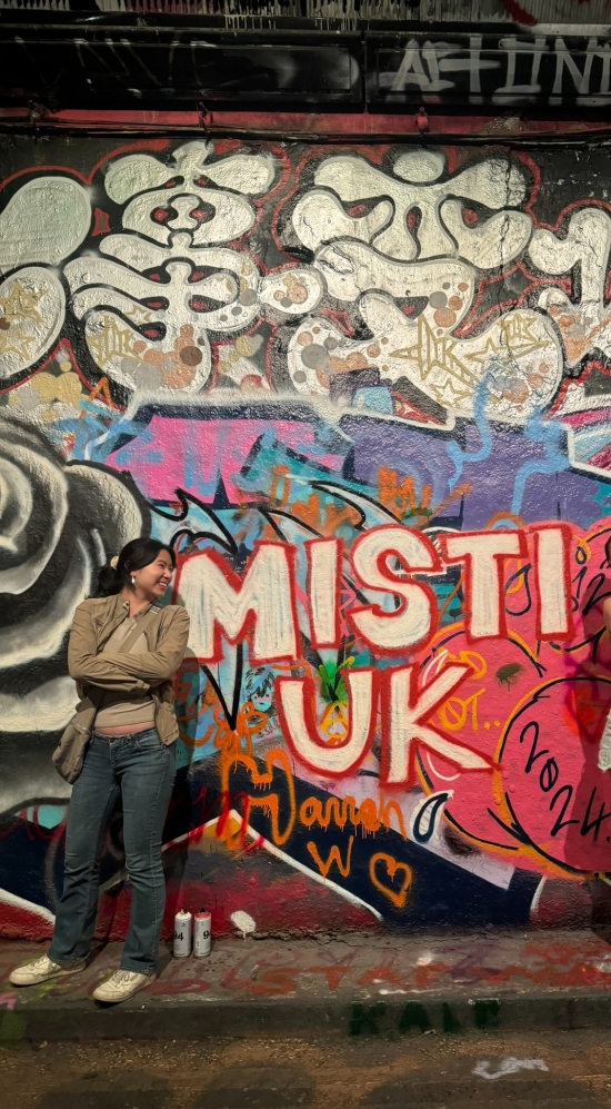 Jocelyn Zhu posing with another MIT friend in front of the a wall filled with murals with MISTI UK