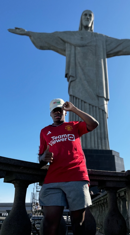 Andre Hamelberg posing in a low angle shot leaning against a stone railing at the bottom of the Christ the Redeemer statue in Brazil on a sunny day with a blue sky