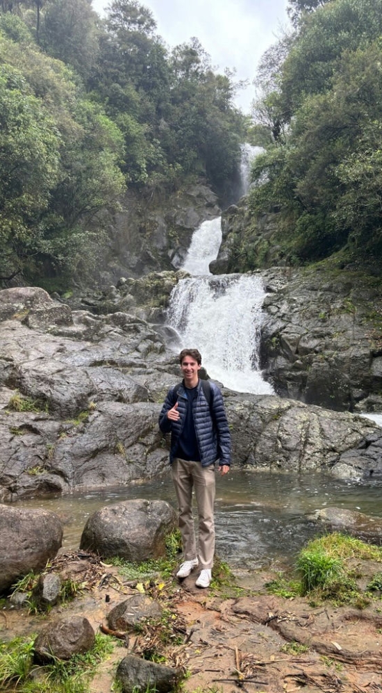 Jensen Fiskin surrounded by tall green trees and a waterfall NZ