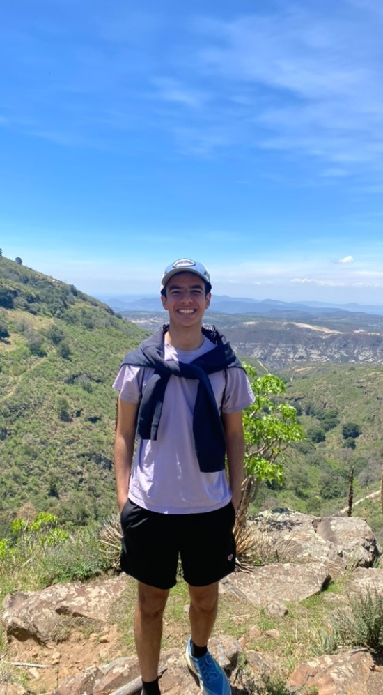 Asael in a cap with a jacket around his shoulders on a hike with a vast background on a sunny day with blue skies