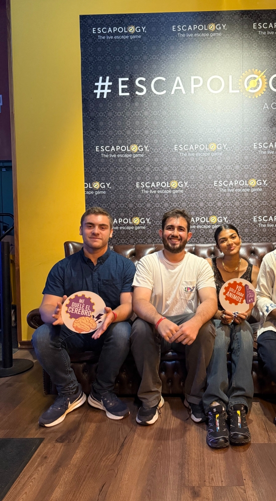 Jace Lopez seated far right with three others on a wooden floor with a sign "#Escapology"