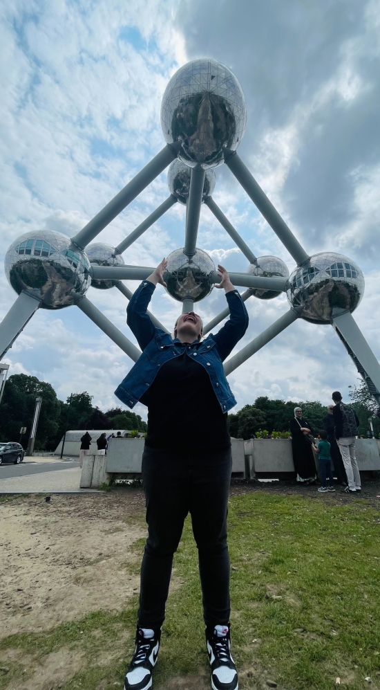A picture illusion of Emilia carrying up an huge atom sculpture under a cloudy sky