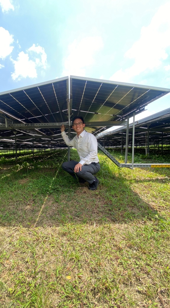 Kevin Yi in a button down shirt squatting below raised solar panels