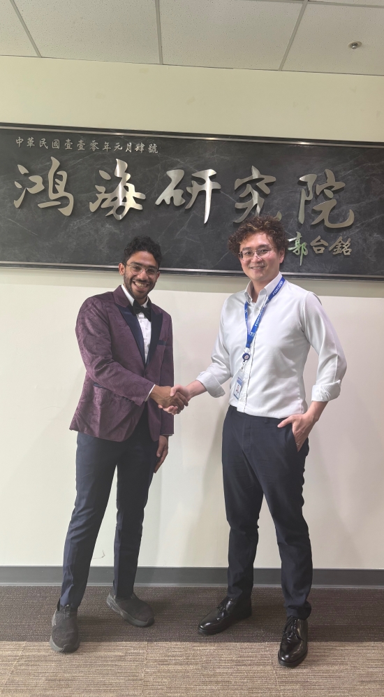 Kumail Al Hamoud shaking hands with a person in front of a white wall and a dark grey plaque with chinese words