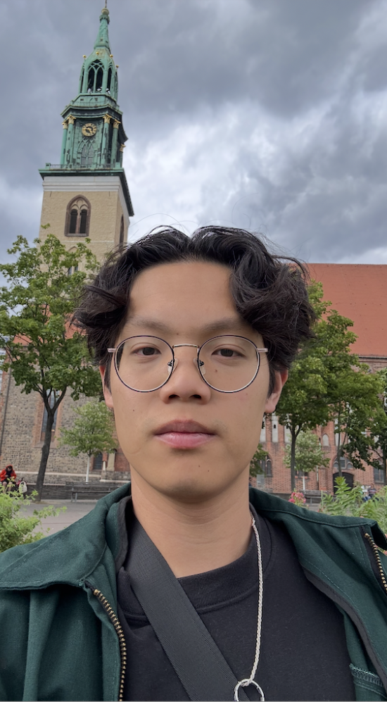 Selfie of Stephen Hong on a cloudy day with a clock tower in the background that has a green ornamental roof