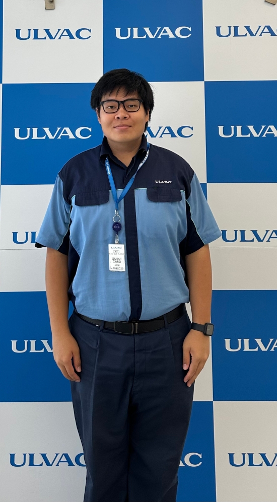 Win Win standing wearing a ULVAC uniform in front of a background with ULVAC's logo