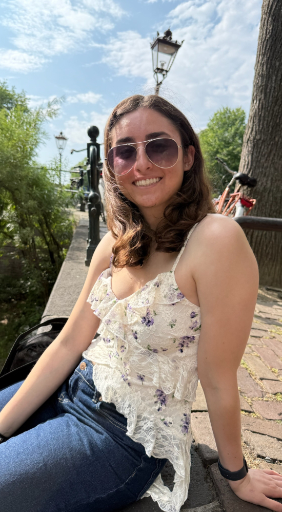 Lisa Vargas in aviator glasses seated on a pedestrian sidewalk with a bike against a tree 
