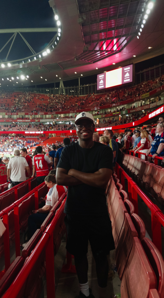 David Sanwo with crossed arms standing in the middle of seats in a stadium