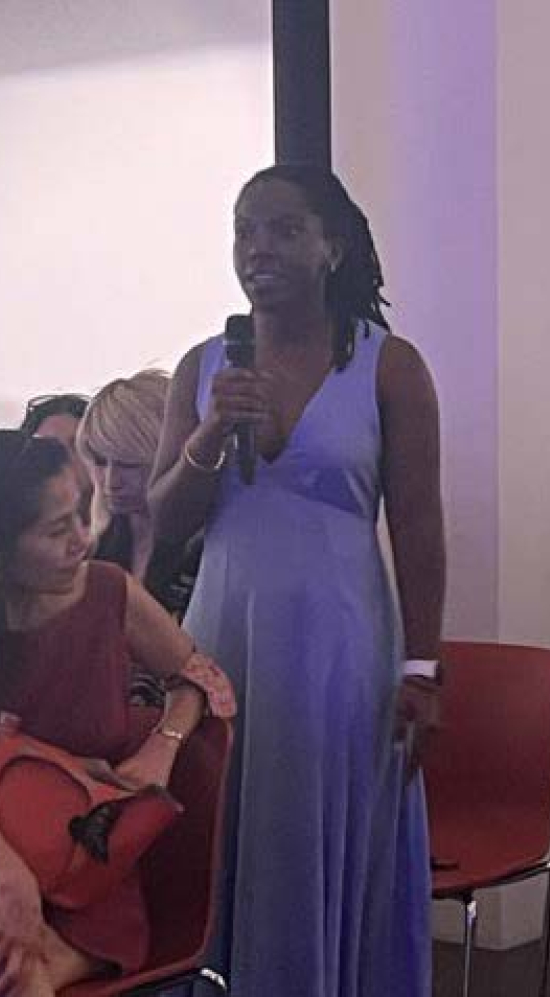 Janae F holding a mic in a room with others seated and looking up at her