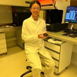 Yijun Yang in a white lab coat and safety glasses in a lab in France