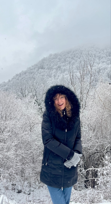 Tatiana Vassiliev in a navy blue winter jacket with a furry hood up out in a forest covered with snow in Armenia 