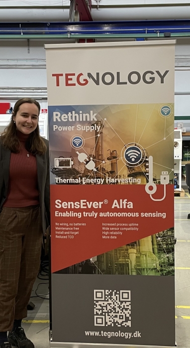 Dahlia stands next to Tegnlogy poster in the lab