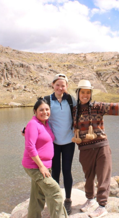 Alison Rufo standing with two locals on a rock overlooking a rocky mountain by the stream