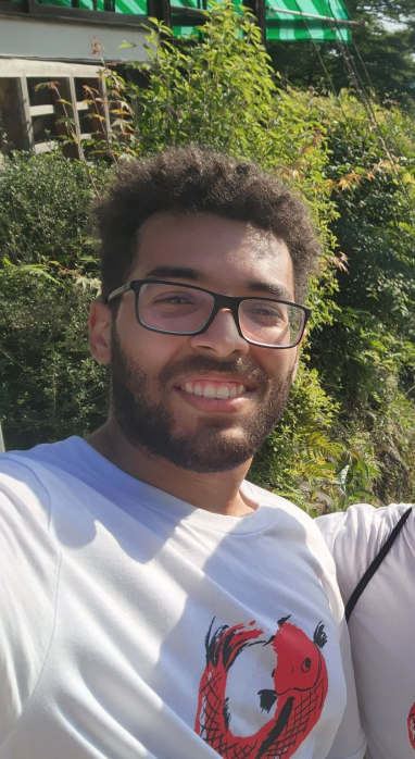 Selfie of Arthur De Los Santos and Daniel from MIT on the steps with a Japanese torii gate in the background and the city skyline