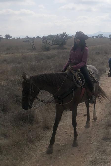 Aniesha Dyce on horseback in Tequisquiapan, Mexico with a background of a cloudy sky and of farmlands