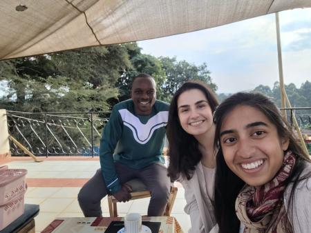 Negin Amouei in the middle of a selfie with Aashini Shah on the right and to the left a local guide at the coffee farm sitting down under a canopy overlooking the coffee farms with lush green trees