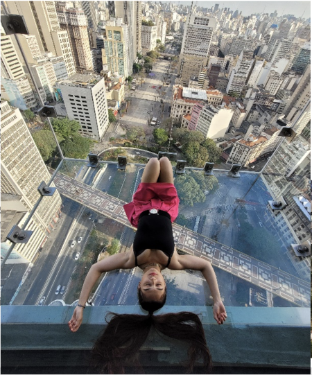 Prathysha laying down on a glass box lookout, Sampa Sky, with a view of the city of Sao Paolo, Brazil