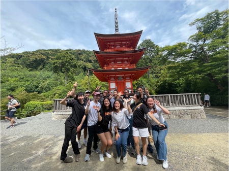 Michael Iglesias and other MIT students posing in front of a red temple with a luscious green trees in the background in Kyoto Japan