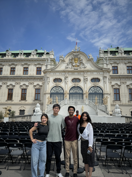 Andy Zheng standing with three other MIT students in front of a off white European building with green roofs and arch windows 