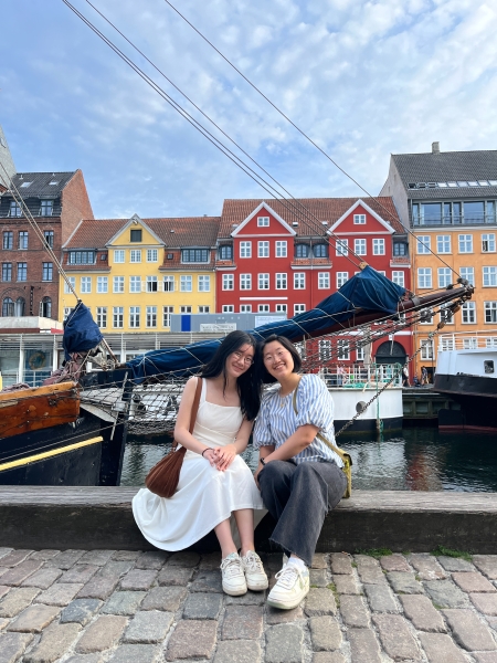 Allison Park seated at the riverbank in front of colorful houses in Denmark