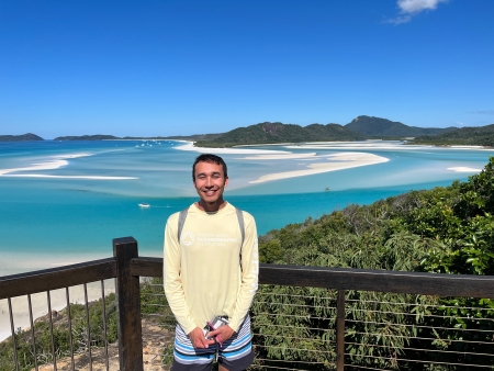 Andrew Motz in a yellow long sleeve shirt with a vast blue sea in the background in Australia